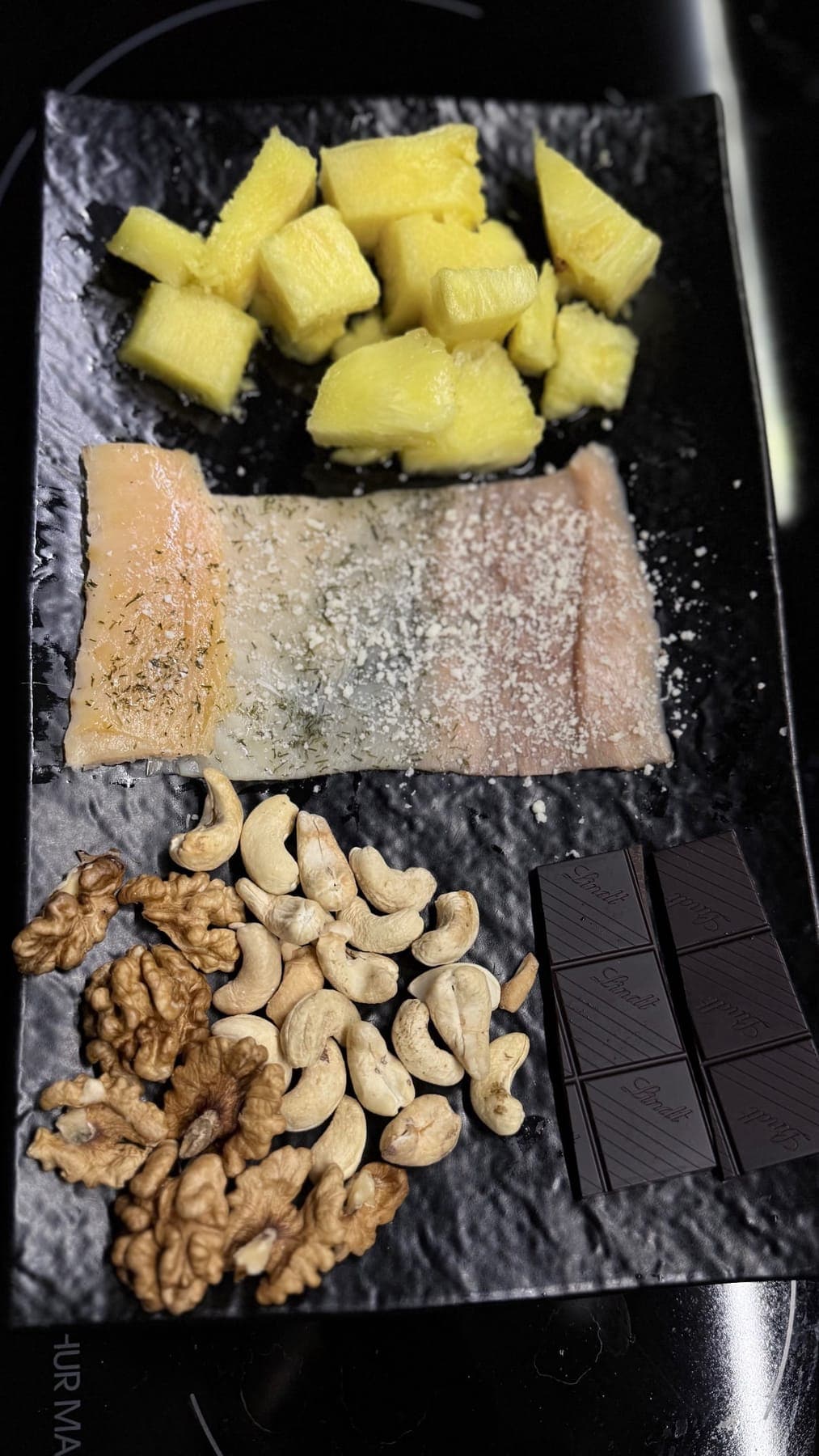 Slate board with fish, fresh pineapple, nuts and dark chocolate