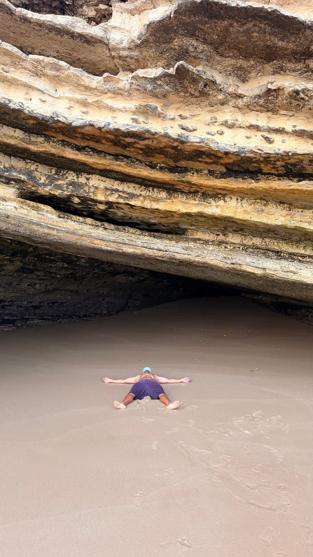 Guest lying on the sand under the rock arch of a secret cave on the Atlantic coast