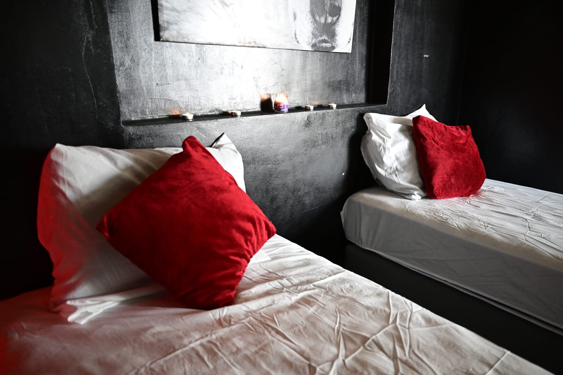 Deux lits simples aux coussins rouges, bougies allumées sur la niche murale